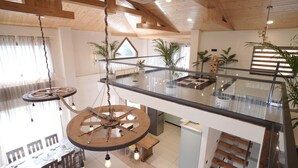 A spacious interior with a high ceiling, wooden beams, a glass railing, and multiple potted plants. - Escape to Amber Moon – Private Luxury Villa in Kumarhatti (Dharampur)