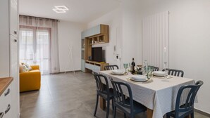 A modern dining area with a table set for four, a sofa, and a TV in the background. - Lovely apartment for 6 guests with WIFI, A/C, TV and patio (Viareggio)