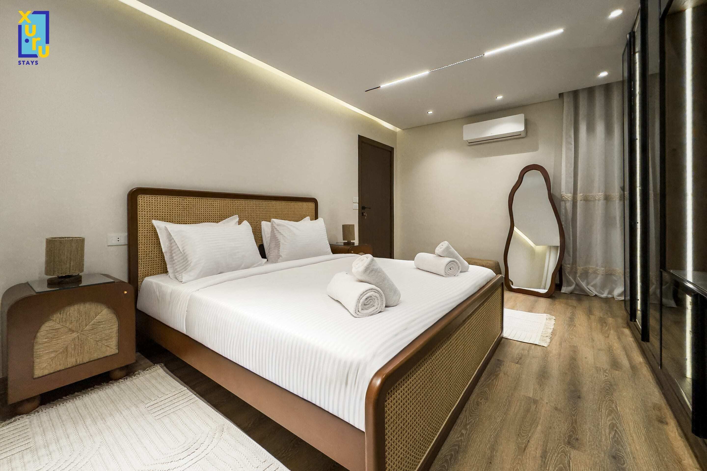 A modern hotel room with a large bed, a bedside table, a mirror, and a view of the city.