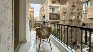 Ein Balkon mit zwei Korbstühlen, Fliesenboden und Blick auf angrenzende Gebäude mit Balkonen und Klimaanlagen.