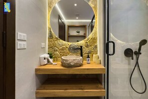 A bathroom with a stone wall, a wooden vanity, a round sink, a handheld showerhead, and a mirror. - Comfy & Cozy 1bdr @ Heart of Heliopolis (Cairo)