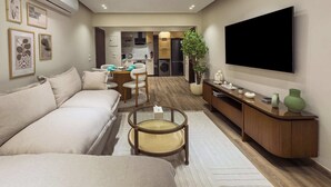 Ein modernes Wohnzimmer mit Sofa, Couchtisch, Fernseher und einer Küche im Hintergrund.