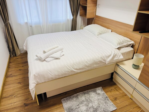 A neatly made bed with white linens and towels, a bedside lamp, and a wooden nightstand.