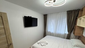 Un dormitorio con cama, televisor de pantalla plana en la pared y ventana con cortinas.