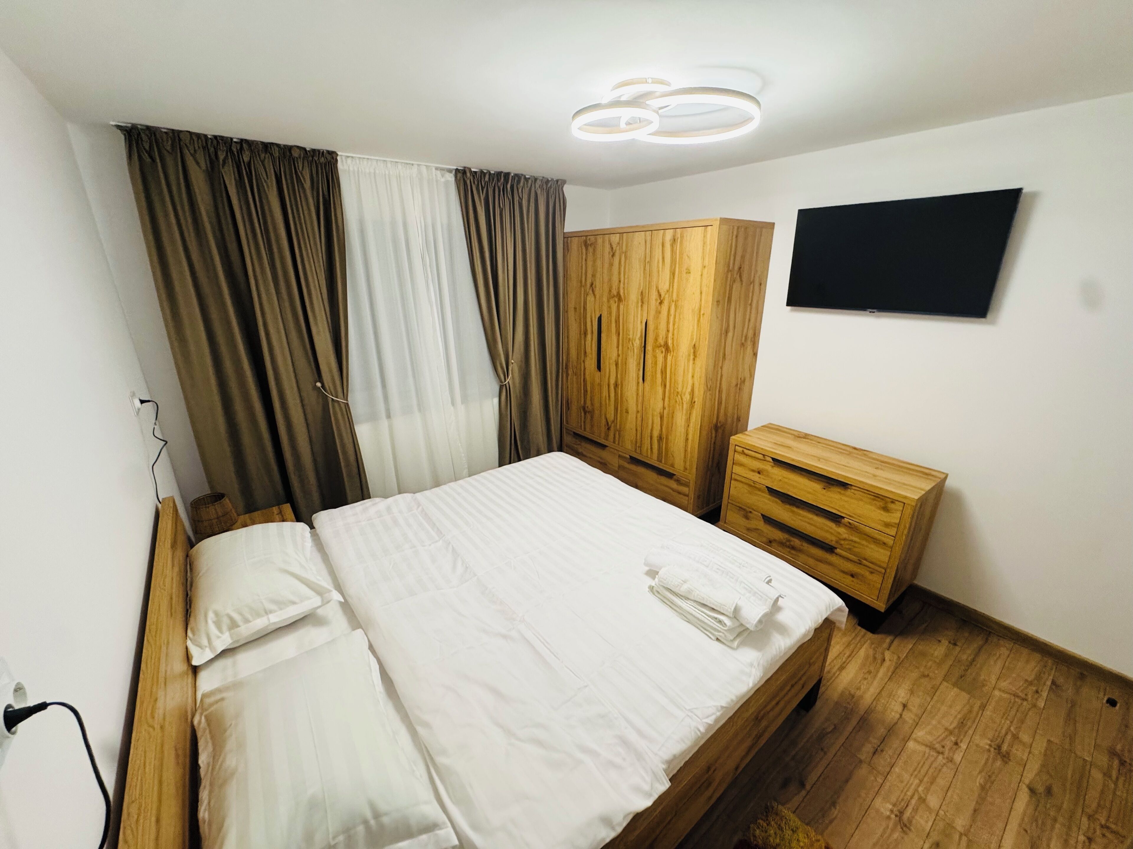 A bedroom with a wooden bed, a wardrobe, a bedside table, and a TV mounted on the wall.