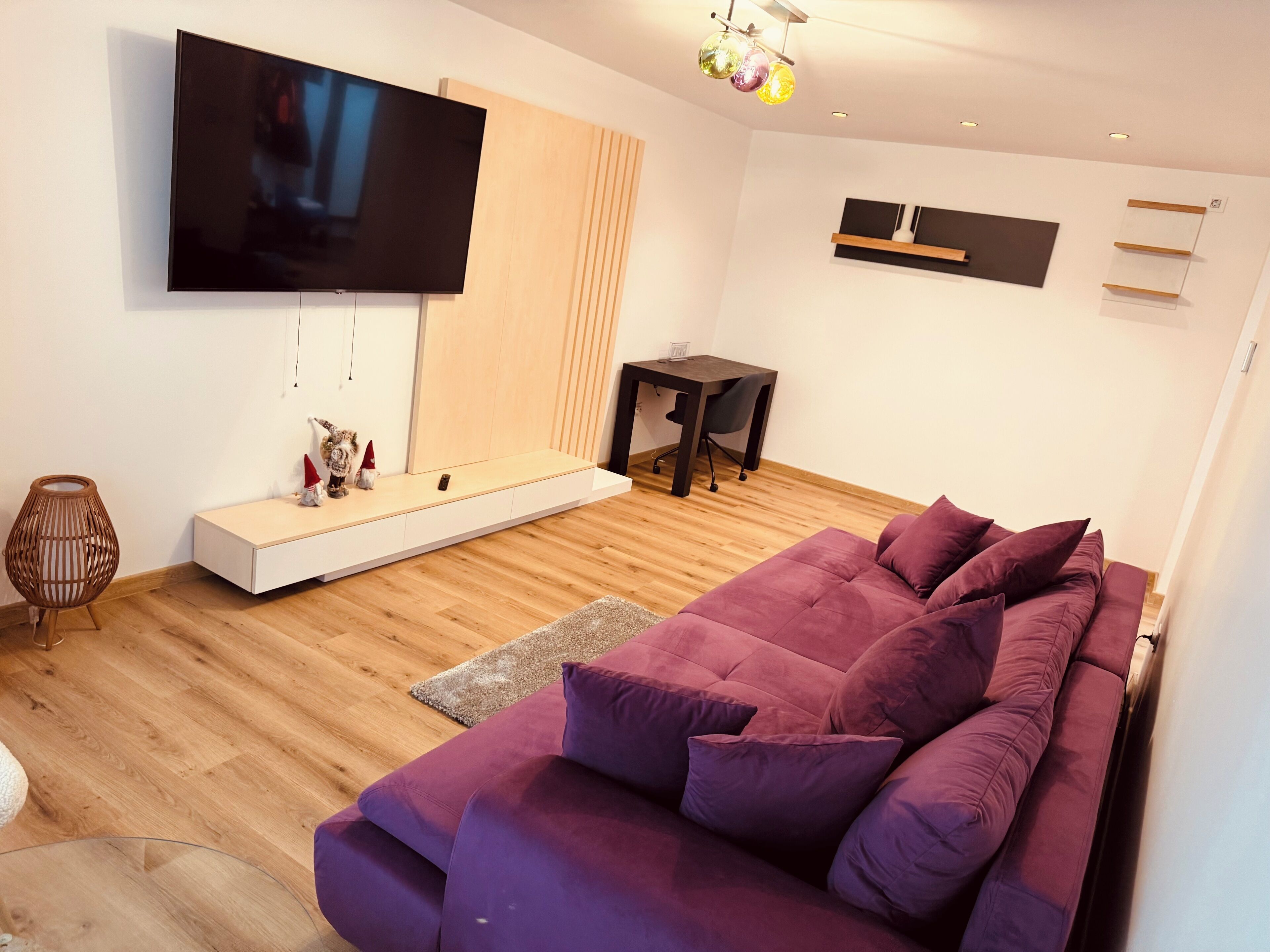 Un salon moderne doté d’un grand téléviseur à écran plat, d’un parquet, d’un canapé violet et d’une petite table avec une chaise.