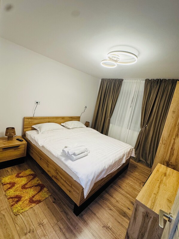 A neatly arranged bedroom with a wooden bed, a bedside table with a lamp, and a wooden nightstand.