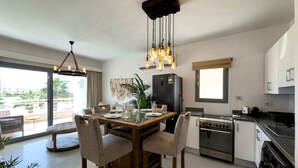 A modern kitchen with a dining area, featuring a wooden table, chairs, a refrigerator, stove, and a sink. - Genial 2bdr @ Swan Lake El Gouna (El Gouna)