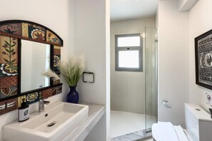 A bathroom with a tiled backsplash, a sink, a mirror, and a shower area.