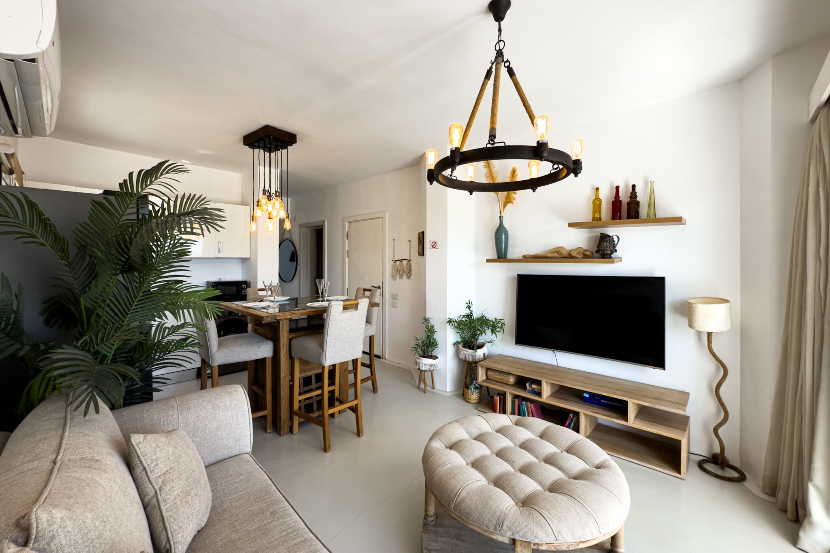 Uma sala de estar moderna com sofá, banqueta, televisão e uma área de jantar com cadeiras e mesa.