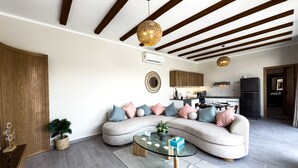 Una sala de estar moderna con un sofá curvo, una mesa de centro de vidrio y una cocina al fondo.