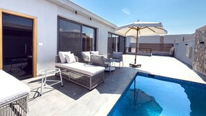Un área de piscina en la azotea con una tumbona, una mesita y un gran parasol.
