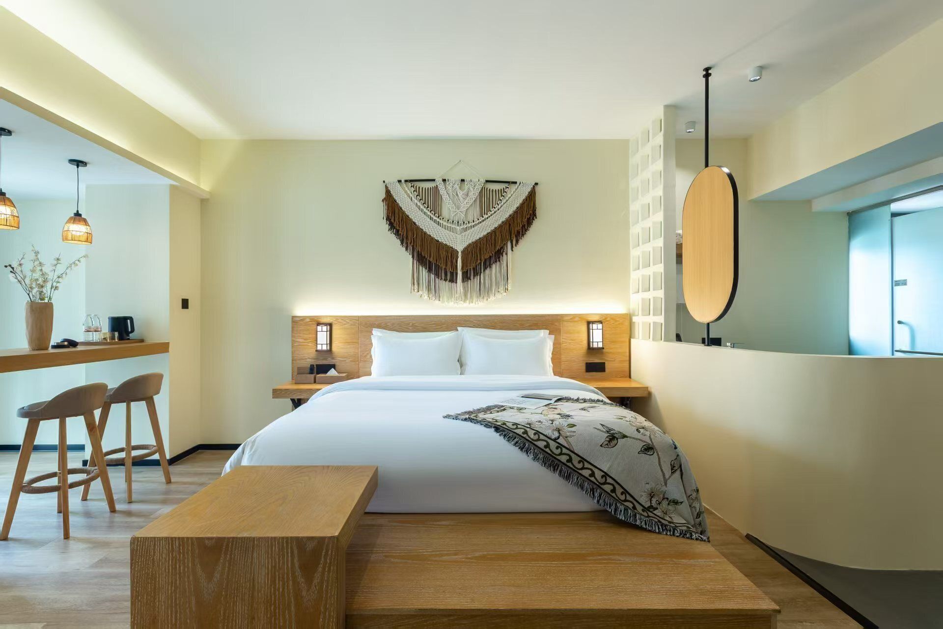 Habitación de hotel moderna con una cama grande, cabecera de madera, mesitas de noche, un banco y una decoración de macramé colgando en la pared.