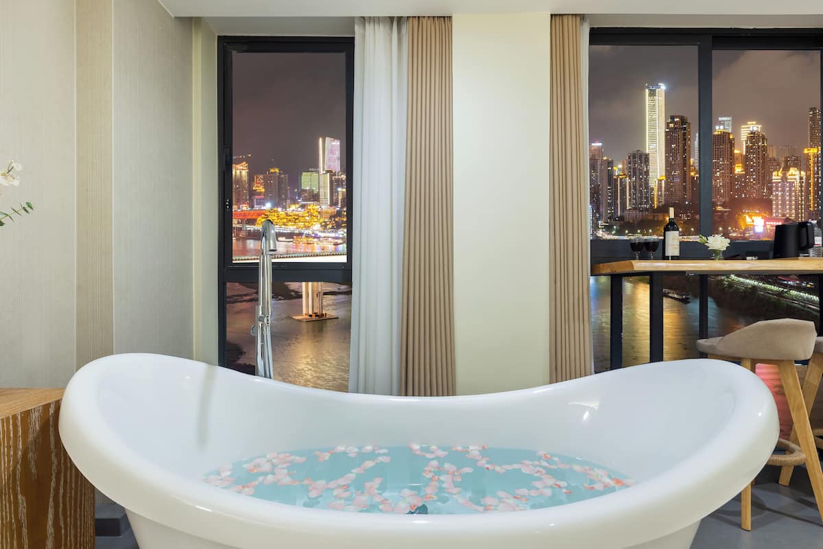 A modern bathroom with a freestanding bathtub, a view of a cityscape at night, and a dining area with a table and chairs.