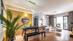 A modern living room with a wooden accent wall, a round mirror, and a dining area with a bench and table. - Deer's Return - Riverside Summer Homestay - Beibin Road (Chongqing)