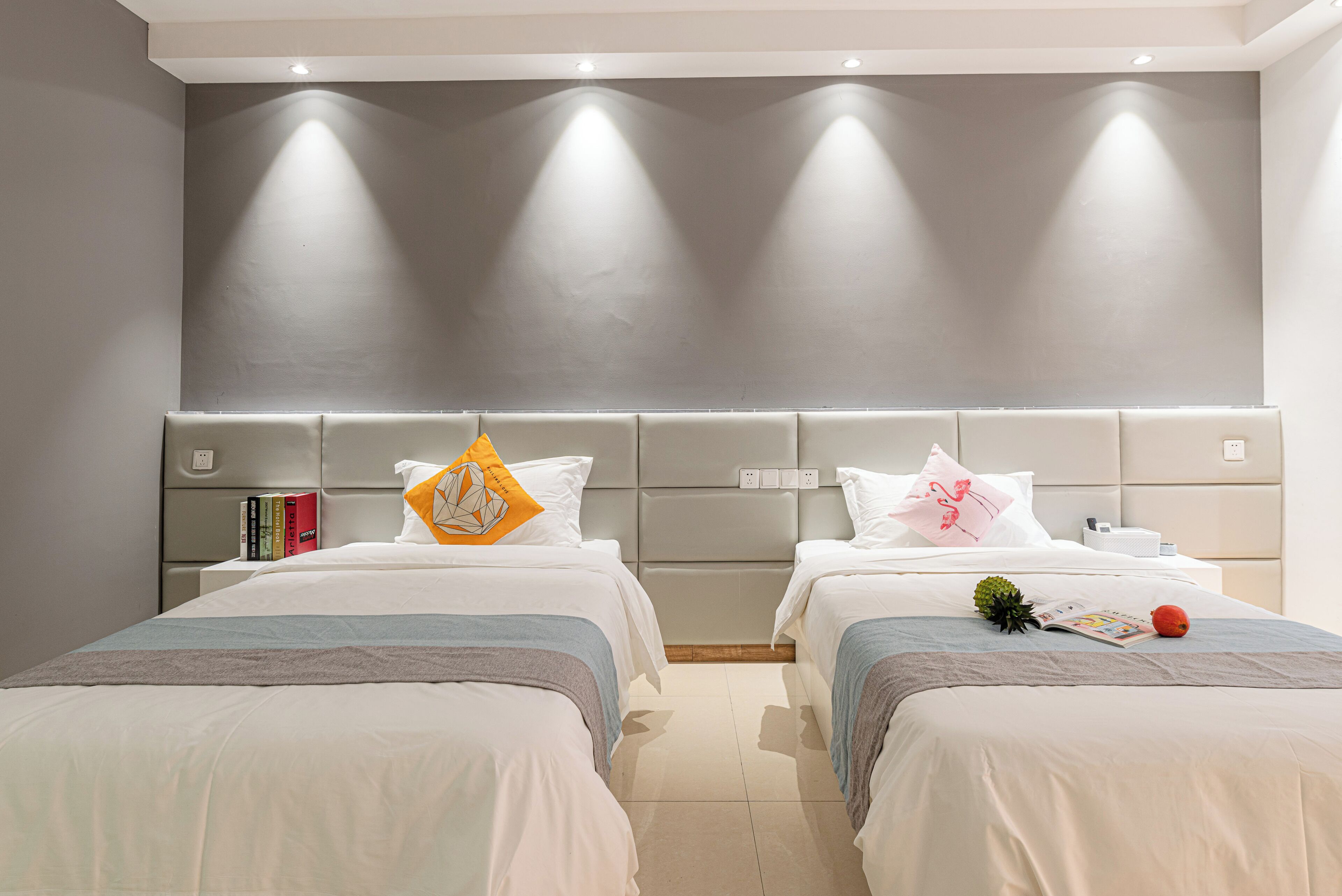 Een moderne hotelkamer met twee bedden, een grijs hoofdeinde en een neutraal kleurenschema.