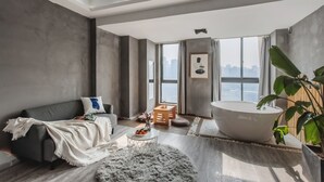 A modern living room with a large bathtub, a grey sofa, and a view of the city. - Deer's Return - Riverside Summer Homestay - Beibin Road (Chongqing)
