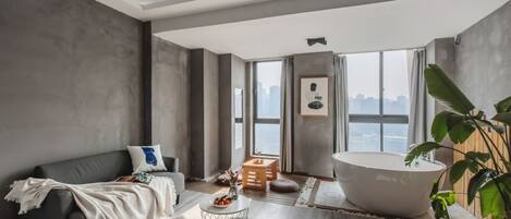 A modern living room with a large bathtub, a grey sofa, and a view of the city.