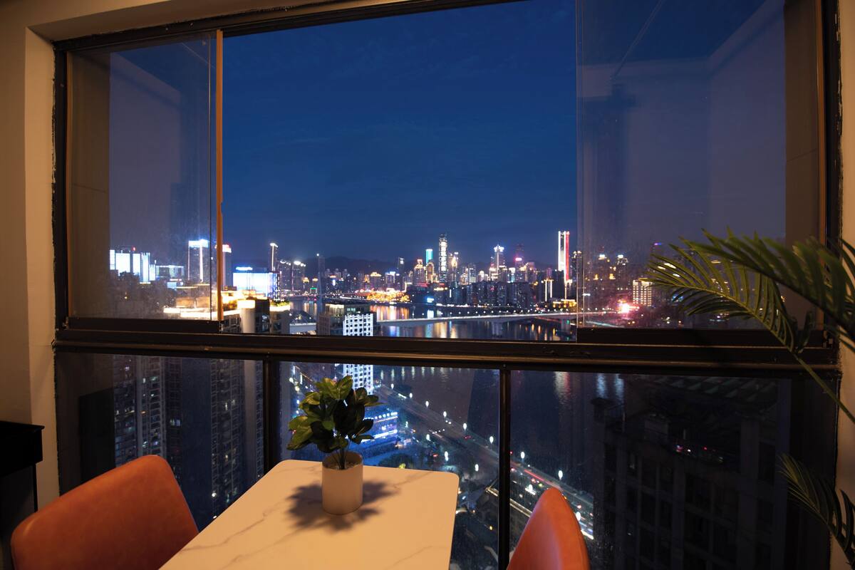 A high-rise room with a city view, a dining table, and two chairs.