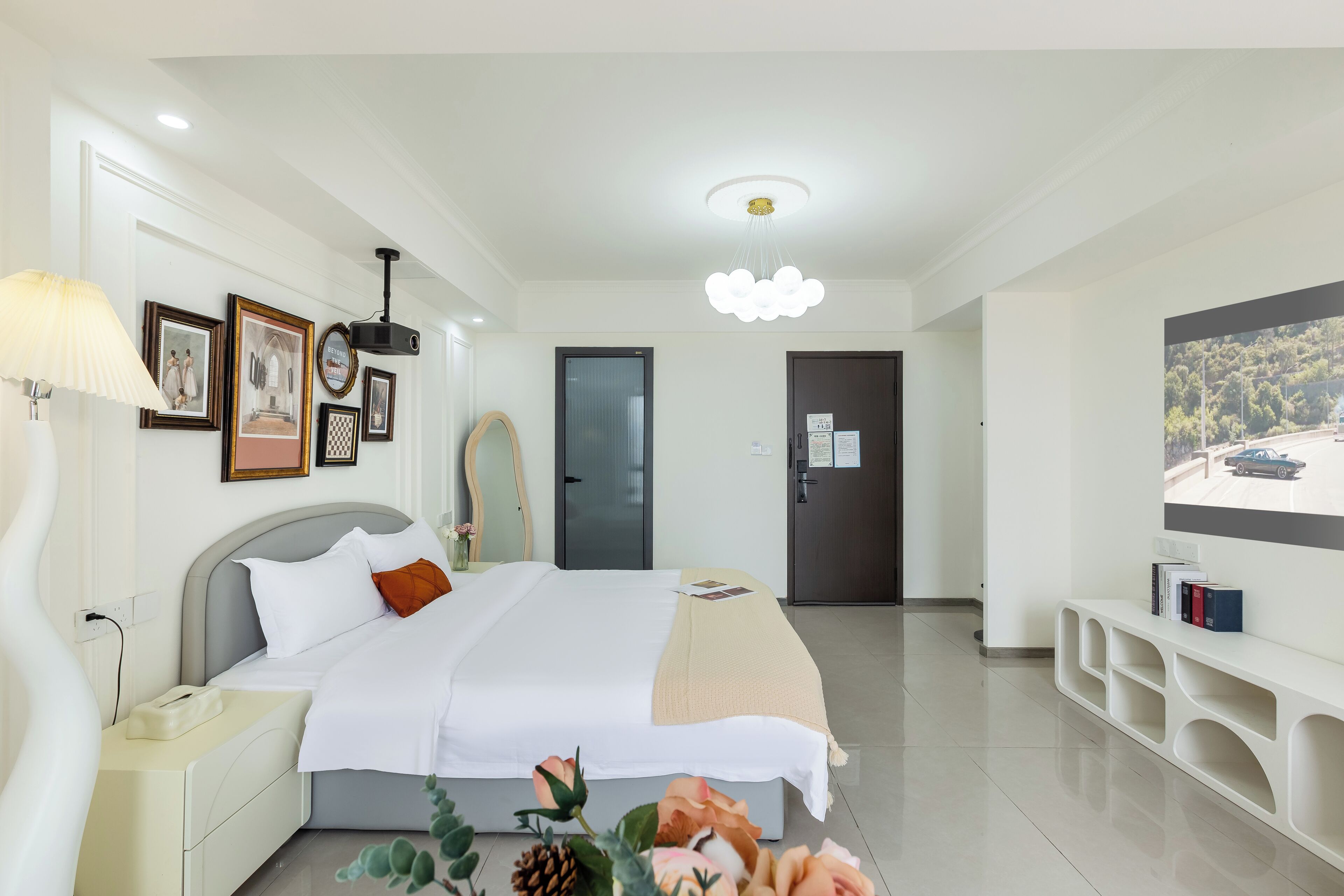 A modern hotel room with a bed, bedside table, lamp, framed pictures, and a TV on a stand.