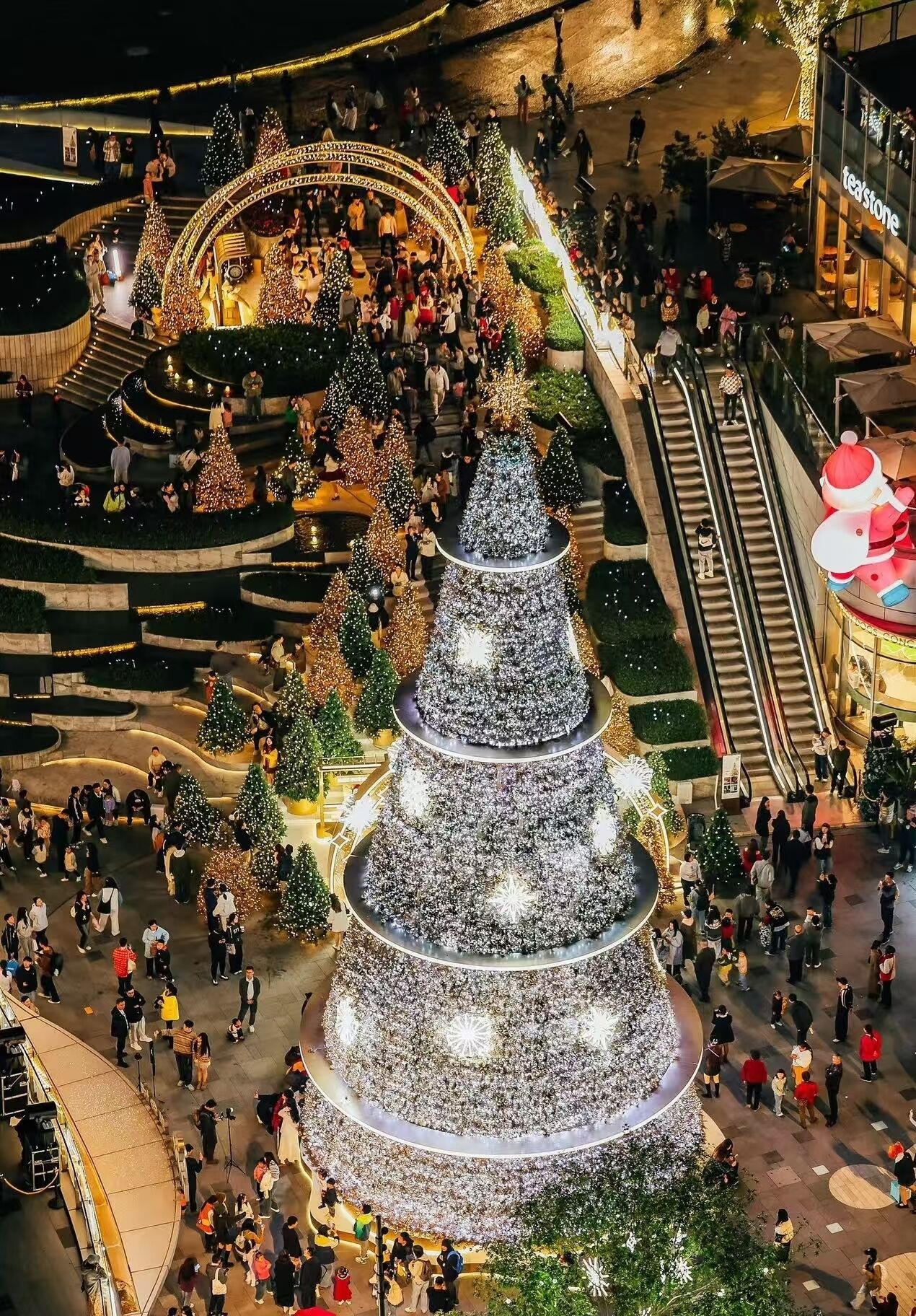 A large, multi-tiered Christmas tree structure surrounded by people.