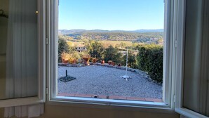 Ein Zimmer mit großem Fenster und Blick auf eine ländliche Landschaft mit Häusern und viel Grün.