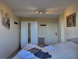 A hotel room with a bed, a door, a coat rack, and a painting on the wall.