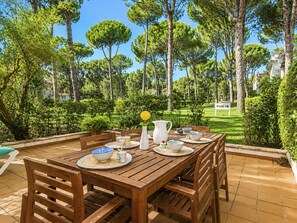 An outdoor dining area with a wooden table set for four, surrounded by chairs, with a view of a well-maintained garden and a sign indicating the direction to the pool. - Country Club Family by Interhome (Pals)
