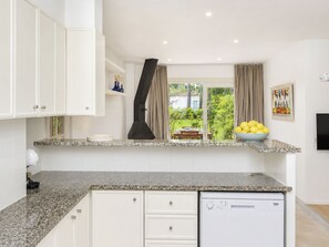 A kitchen with white cabinets, a built-in dishwasher, a window with curtains, and a bowl of lemons on the counter. - Country Club Family by Interhome (Pals)