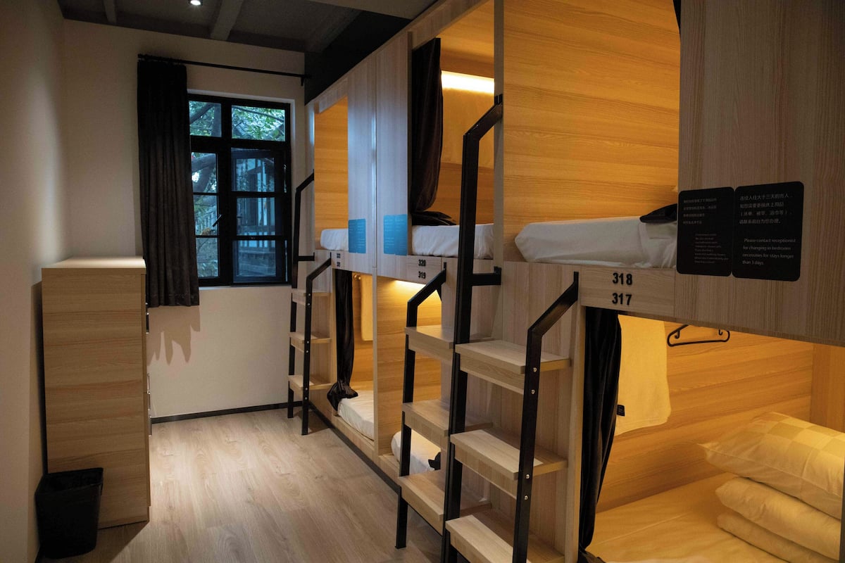 Habitación tipo dormitorio con literas, un escritorio pequeño y una ventana con cortinas.