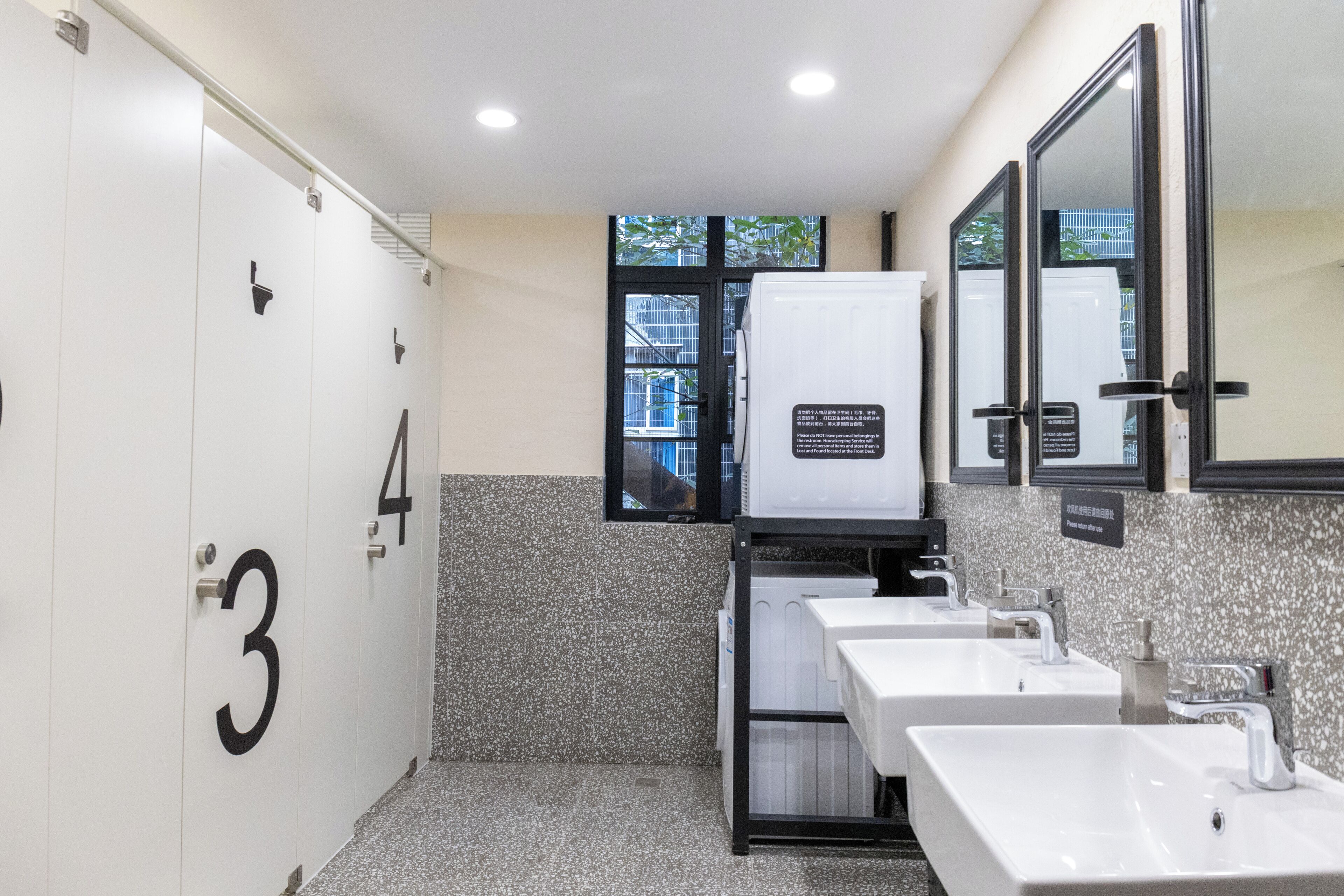 A modern bathroom with white sinks, a large mirror, and a frosted glass window.