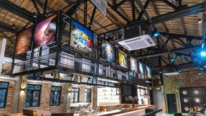 Un área de bar moderna con techo alto, vigas a la vista y una pared de ladrillo rústico.