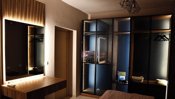 A modern bedroom with a wooden vanity, a large mirror, a wardrobe with glass doors, and a hanging light fixture. - Modern Apartment In City Center (Tiranë)