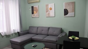 A living room with a grey sectional sofa, a small round table, and three abstract paintings on the wall. - Modern Apartment In City Center (Tiranë)