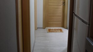 A hallway with a wooden door, a refrigerator, and a light fixture on the ceiling. - Modern Apartment In City Center (Tiranë)