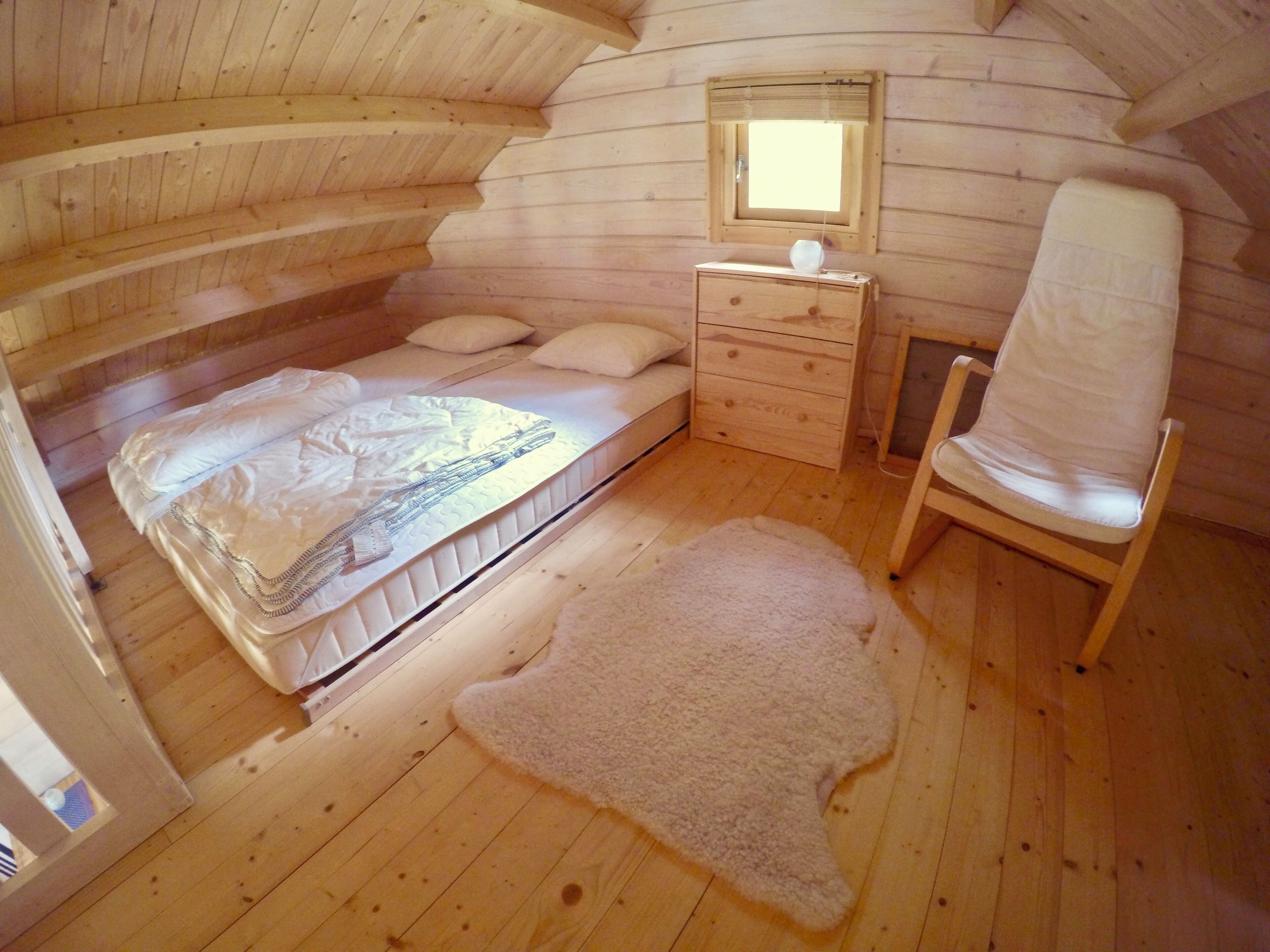 A cozy cabin bedroom with a bed, a chair, a dresser, and a window.