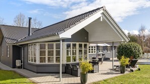 Ein Haus mit überdachter Terrasse, großen Fenstern und Schornstein.