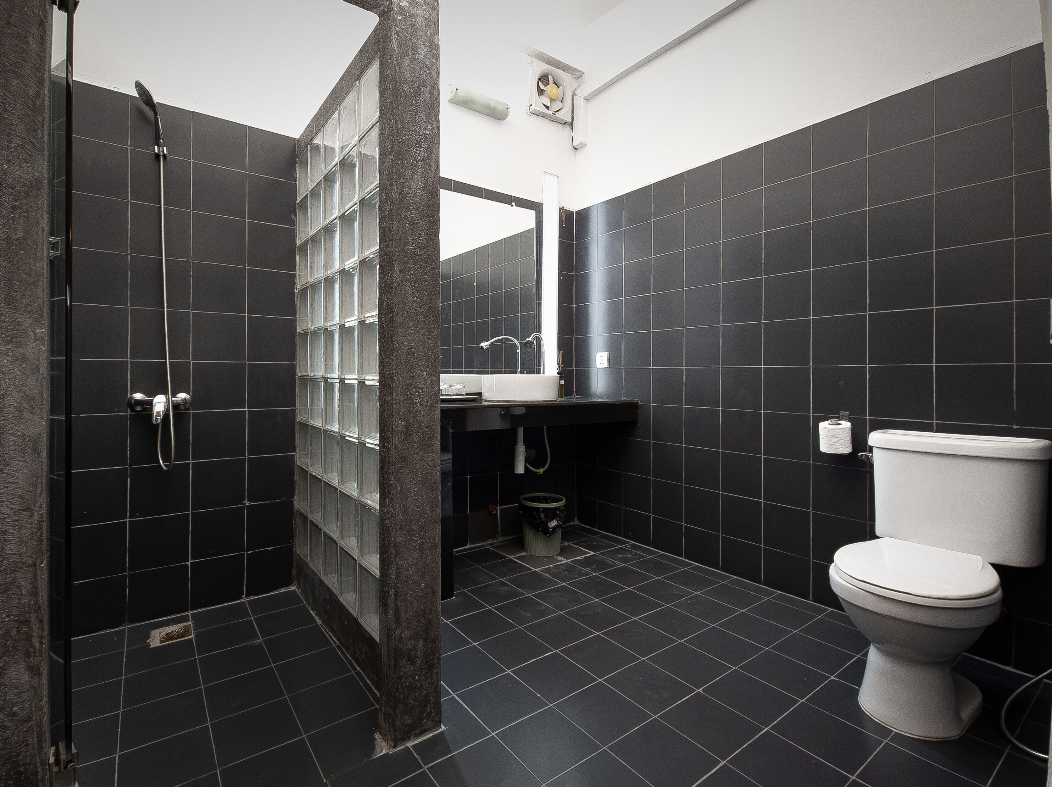 Un baño moderno con azulejos oscuros, ducha, inodoro y lavabo.
