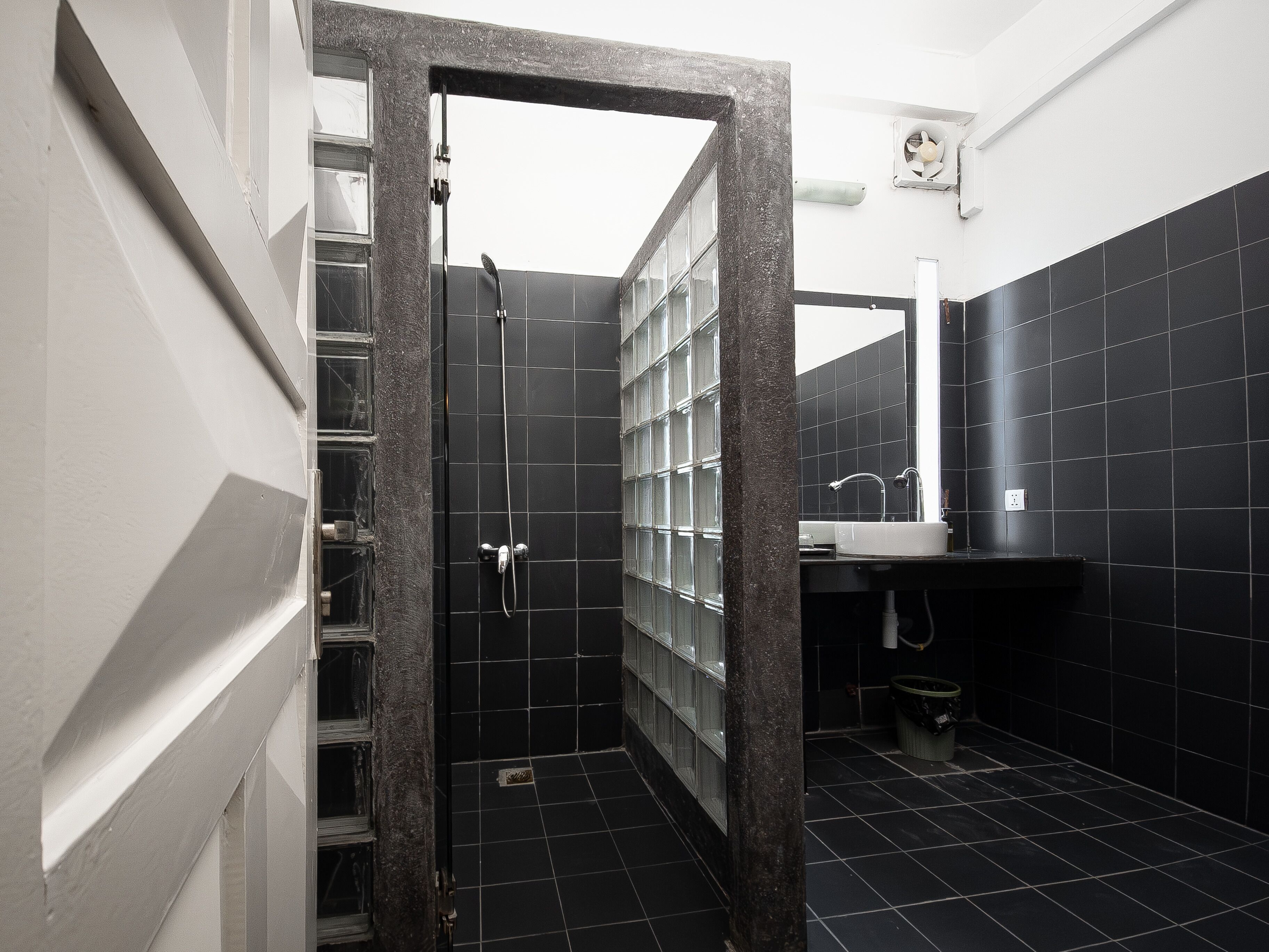 A modern bathroom with black tiles, a glass shower enclosure, and a sink with a mirror.