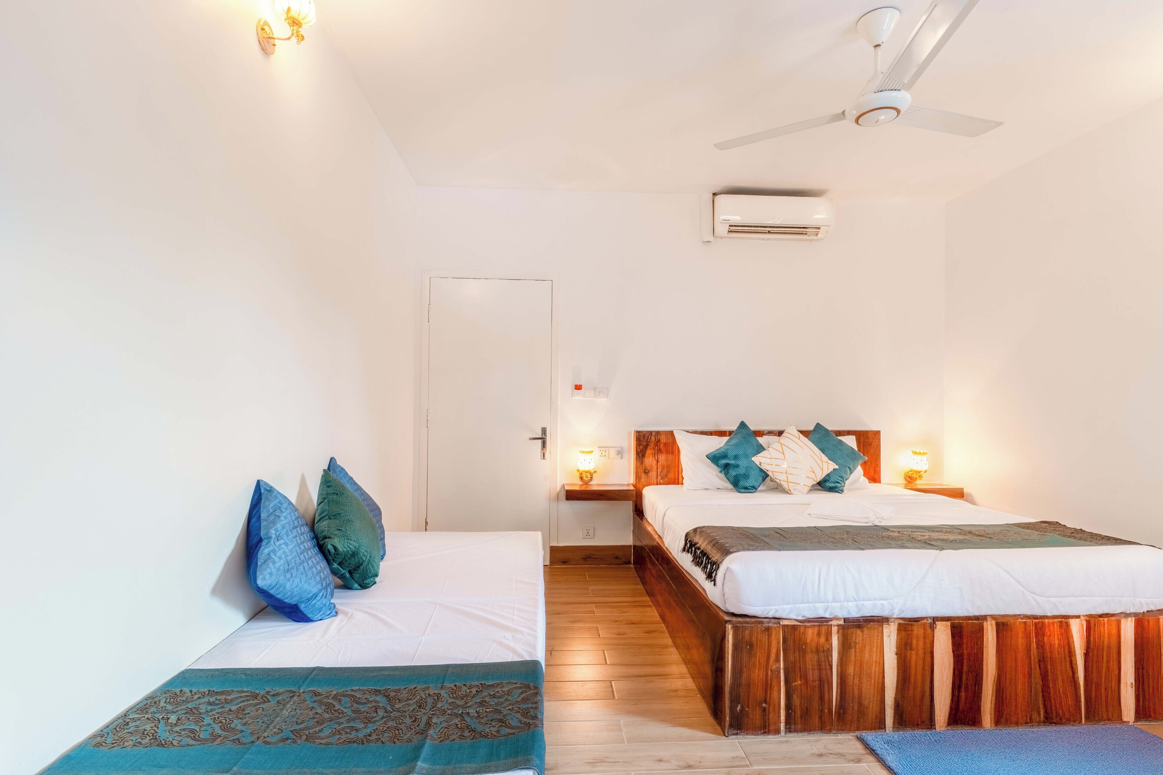 A hotel room with two single beds, a wooden headboard, a ceiling fan, and an air conditioning unit.