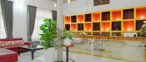 A hotel lobby with a reception desk, a red sofa, a coffee table, and a potted plant.