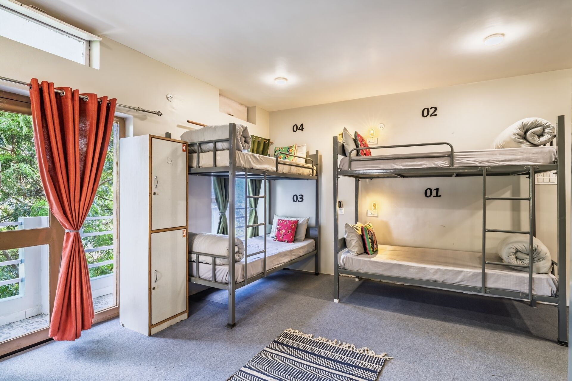 A dormitory room with bunk beds numbered 01 to 04, a wardrobe, and a window with curtains.