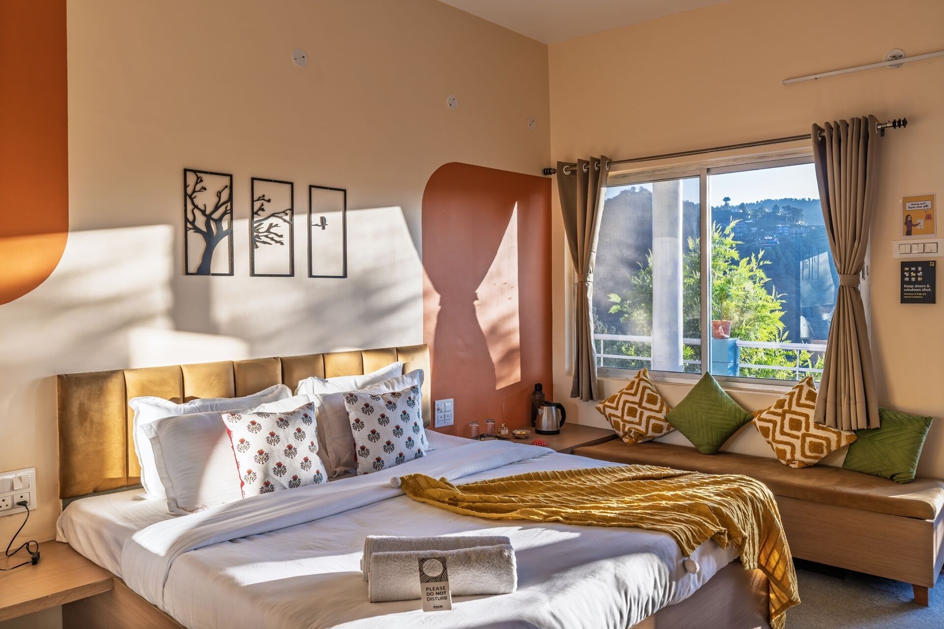 Quarto de hotel com cama, sofá, janela com cortinas e obras de arte nas paredes.