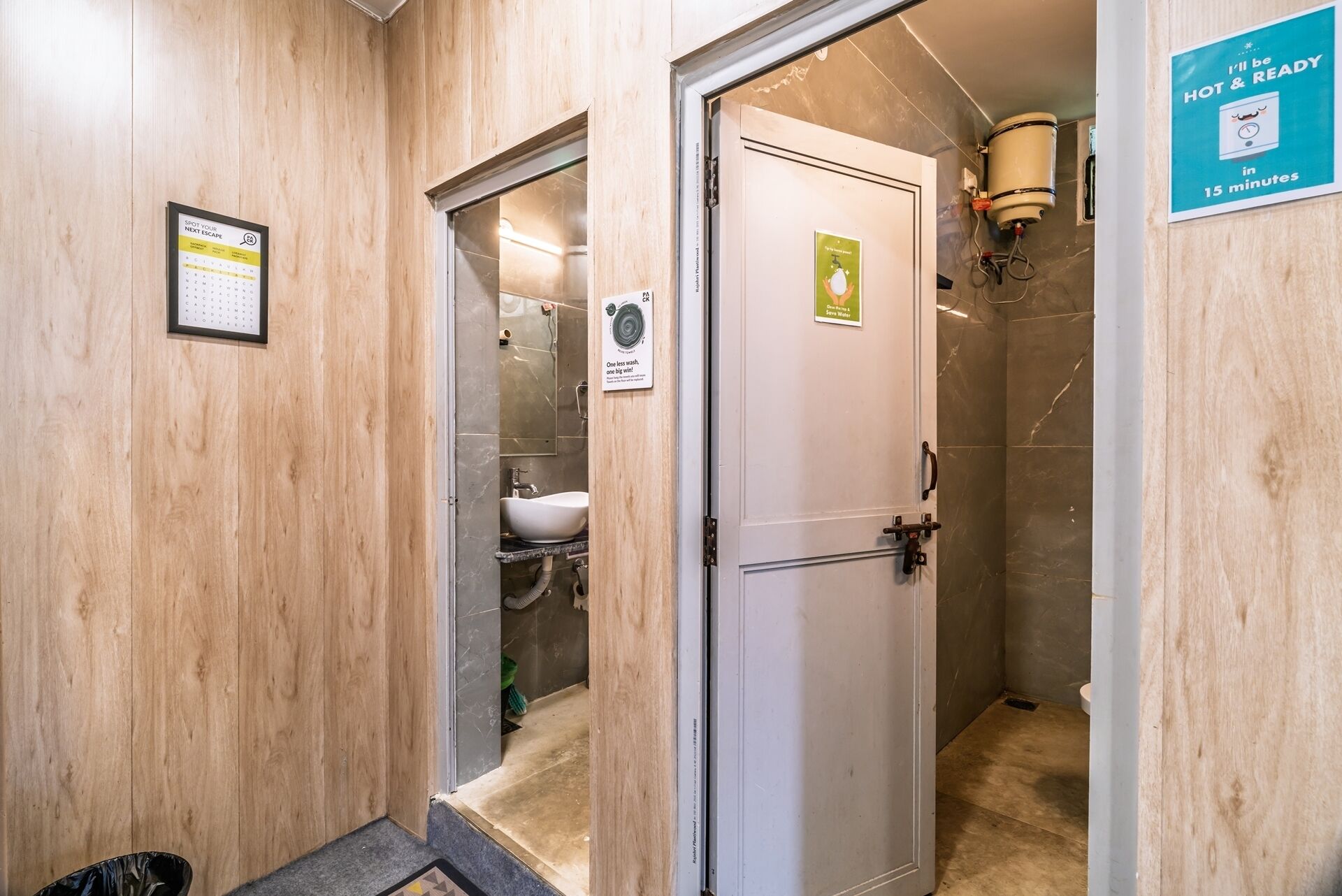 Ein Hotelbad mit Dusche, Waschbecken und Toilette. Ein Schild an der Wand weist auf eine Wartezeit von 15 Minuten für heißes Wasser hin.