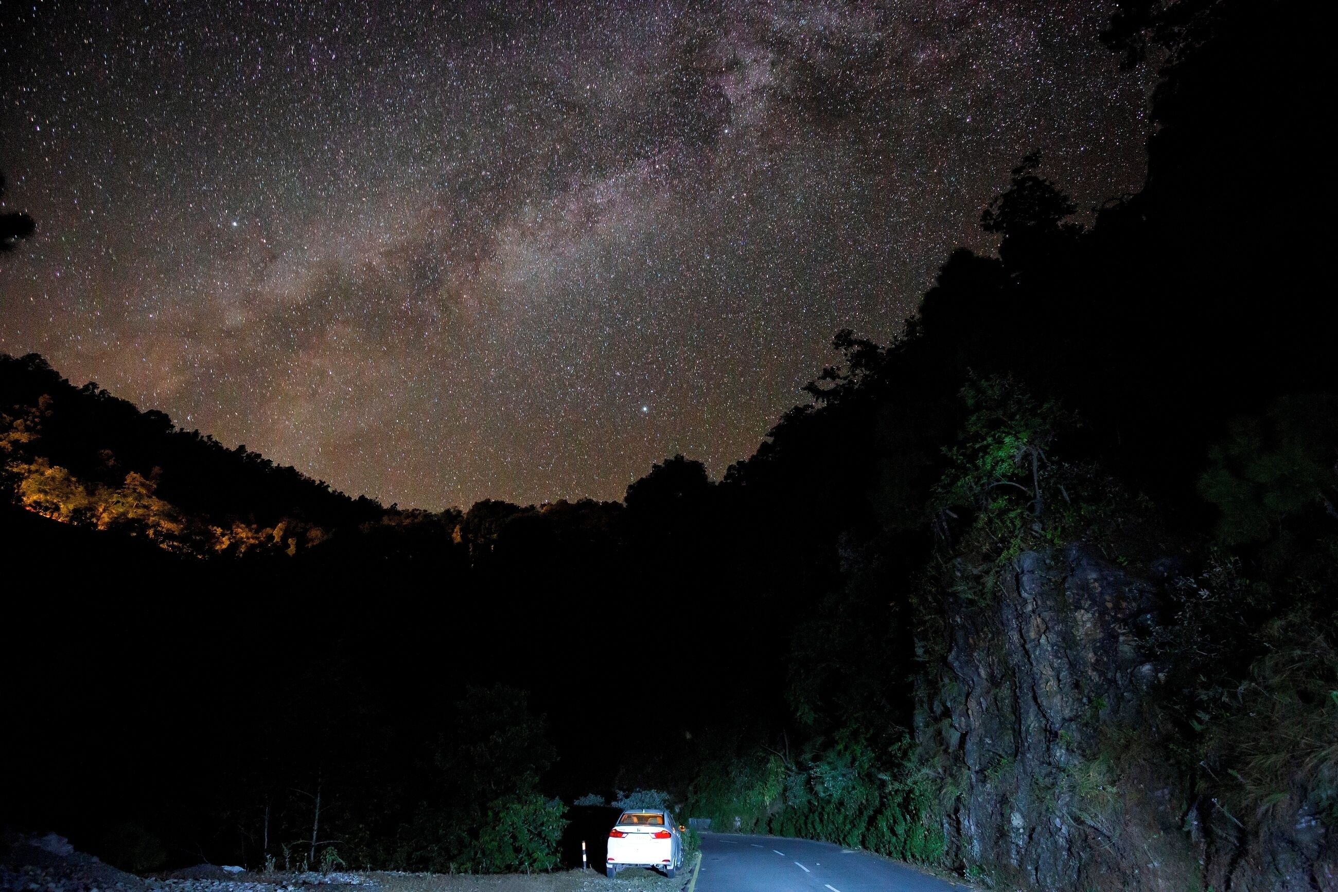 A car parked on a road under a starry night sky.