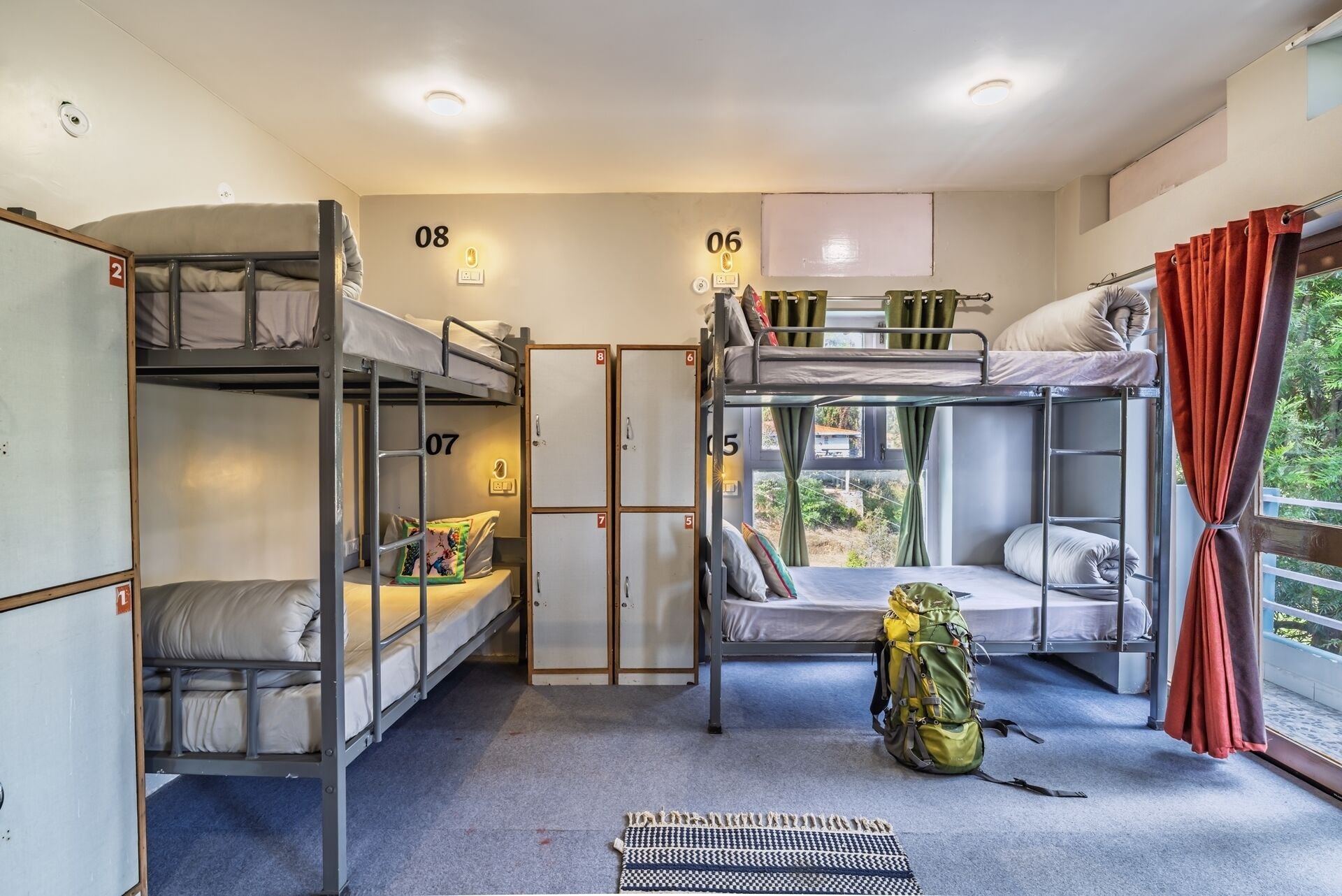 A dormitory room with bunk beds, numbered doors, and a window with curtains.