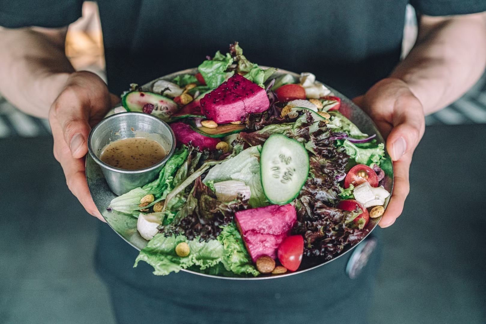 Una persona sosteniendo un bol de ensalada con diferentes verduras y un recipiente pequeño con aderezo.