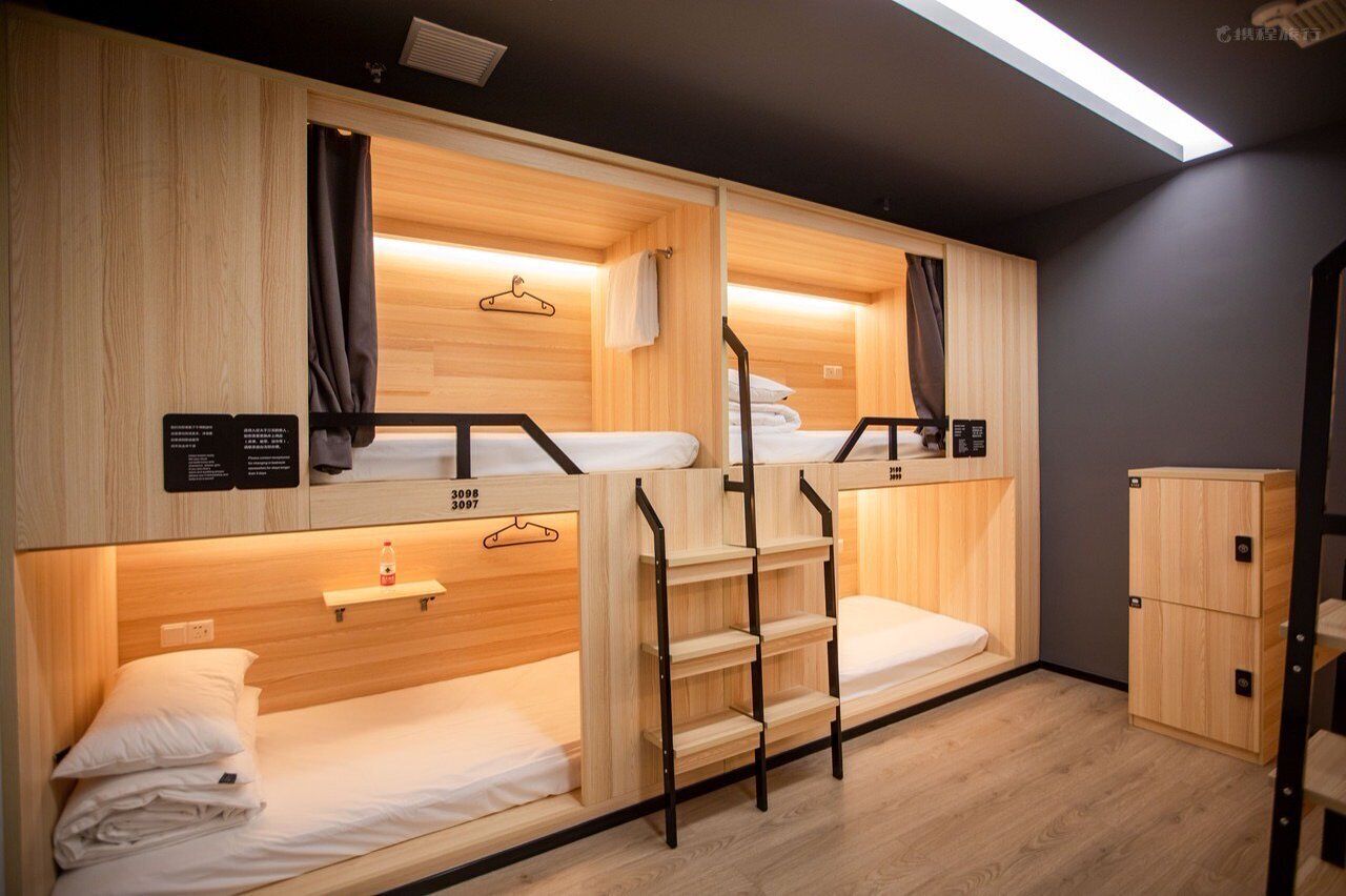 Una habitación de hotel compacta con literas, un armario de madera y un pequeño estante con una botella.