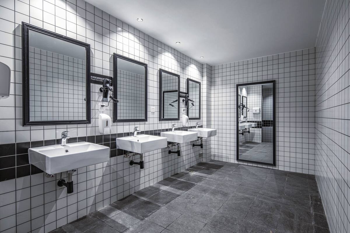 Ein modernes Badezimmer mit drei Waschbecken, schwarzen Rahmen-Spiegeln und Fliesenboden.