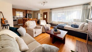 Una sala de estar acogedora con un sofá, sillones, una mesa de centro y una zona de comedor con armarios de madera y una cocina al fondo.